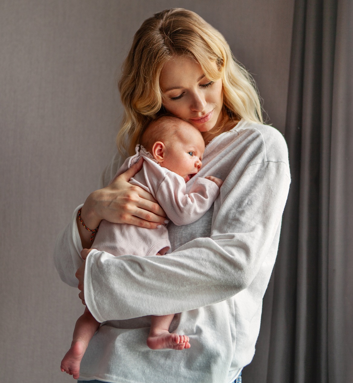 Eine blonde, junge Frau drückt Ihr Baby, liebevoll an Ihre Brust.