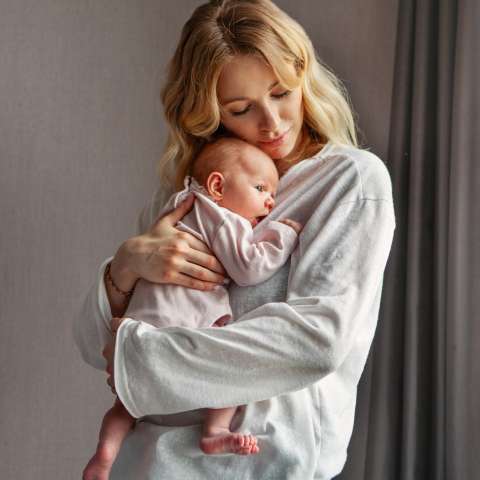 Eine blonde, junge Frau drückt Ihr Baby, liebevoll an Ihre Brust.