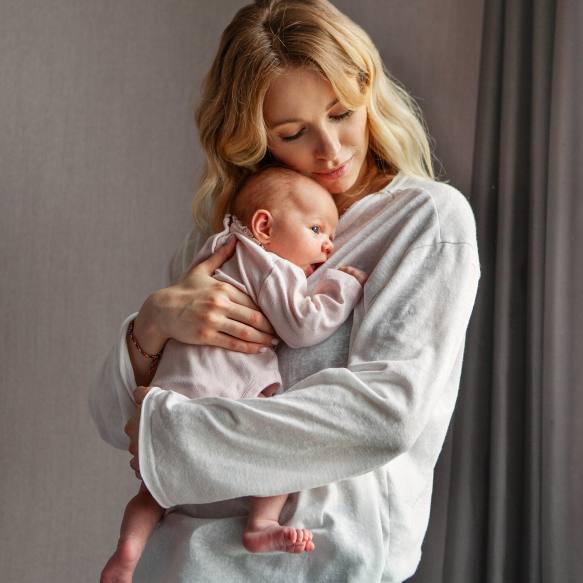 Eine blonde, junge Frau drückt Ihr Baby, liebevoll an Ihre Brust.